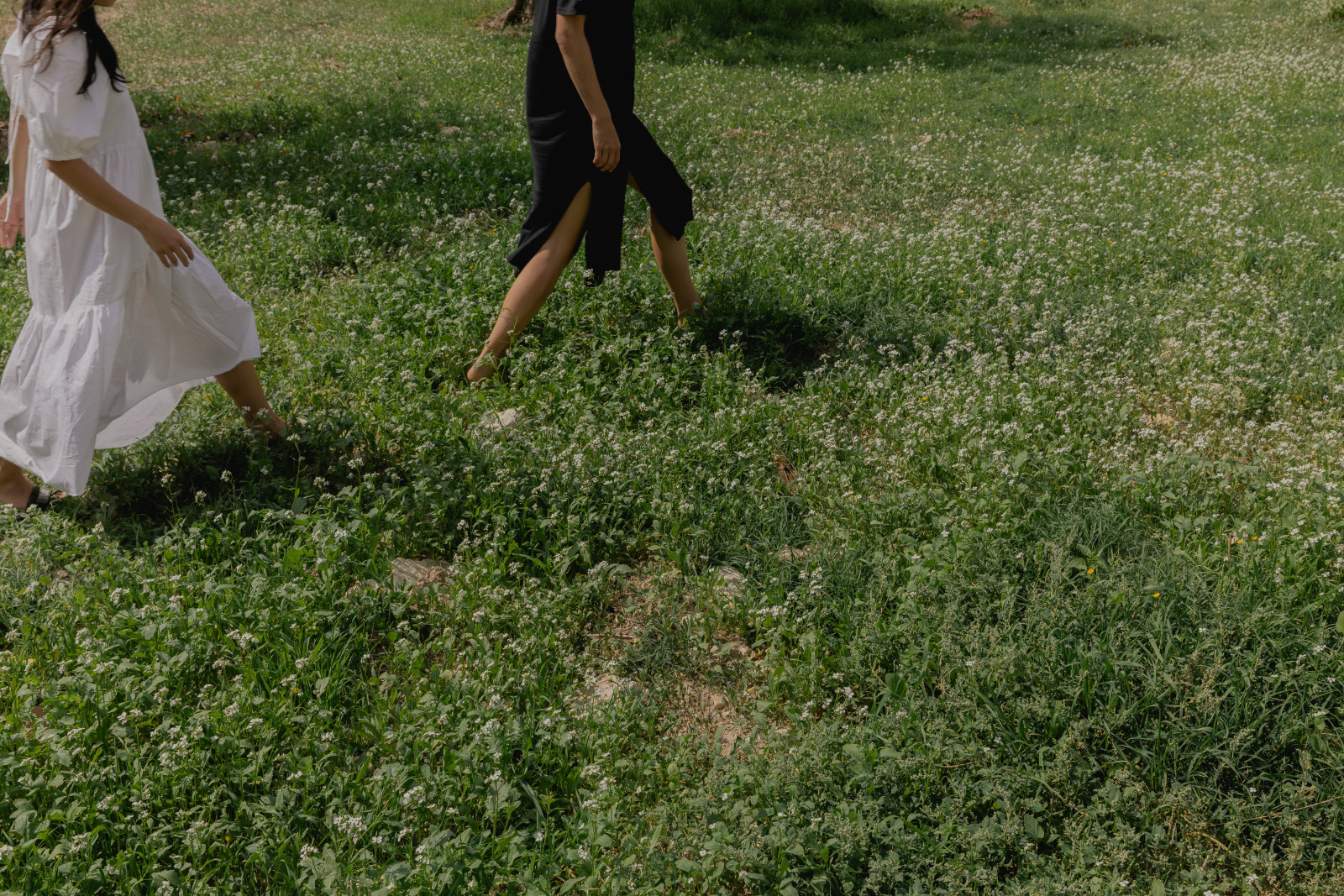 Two women walking barefoot through a wildflower meadow