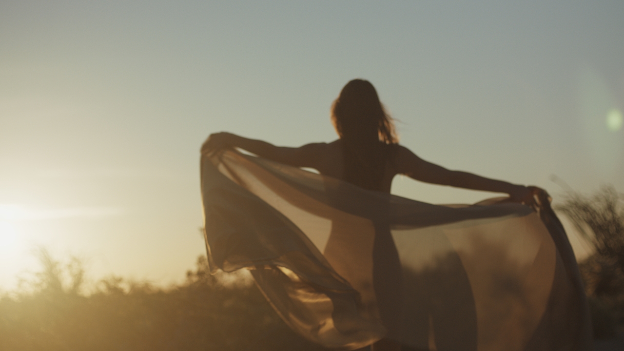 A figure at desert sunrise, sheer fabric catching the wind