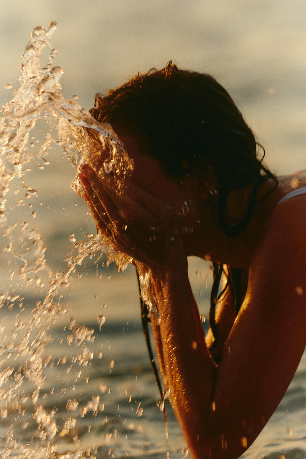 A person rinsing their face in golden ocean light